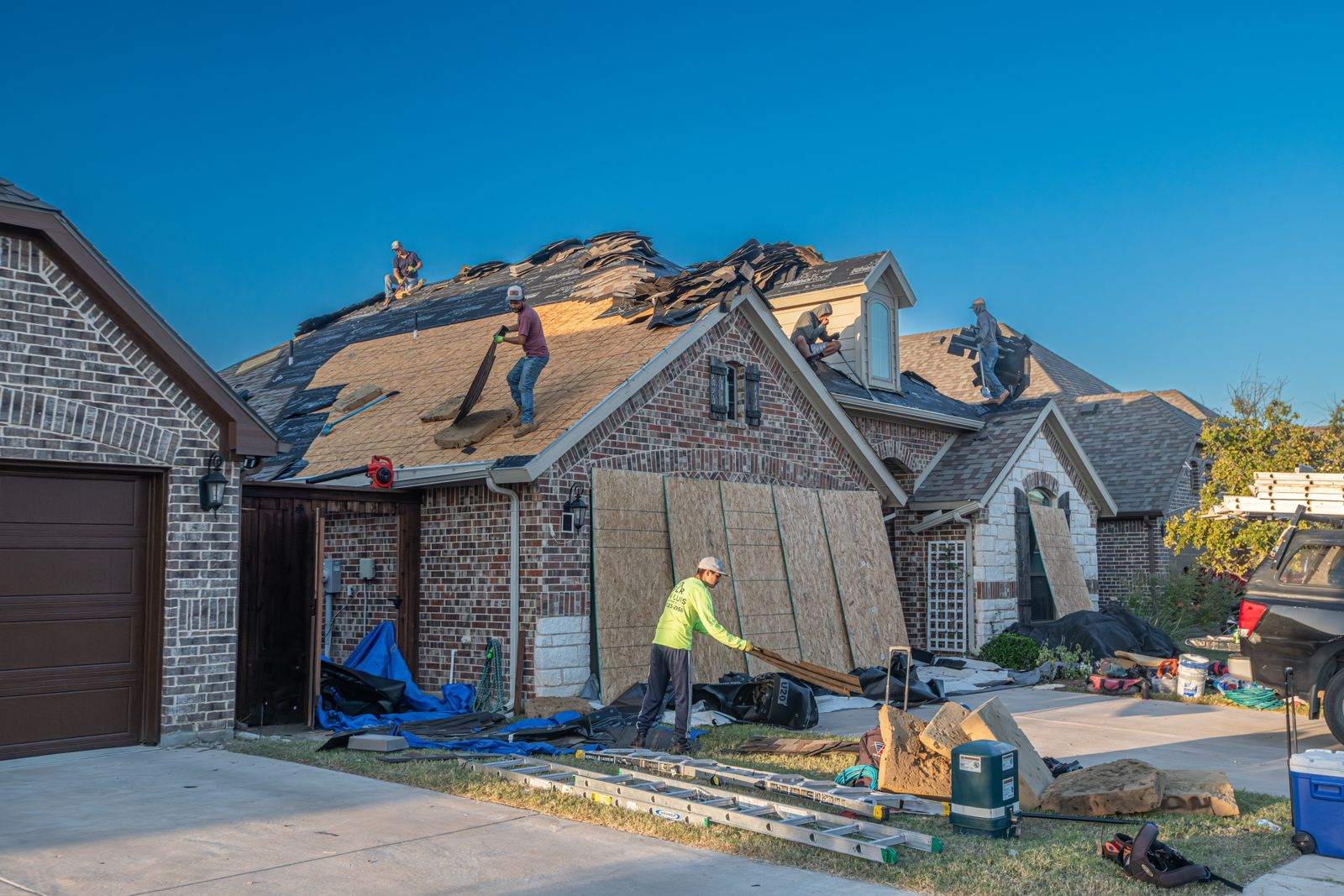 A roofing crew repairing storm-damaged shingles on a house roof with workers on the roof